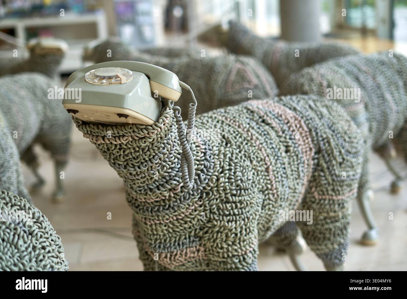 A whimsical art installation featuring sculptures of sheep constructed from vintage telephone cords and rotary dial handsets. The foreground sheep... Stock Photo