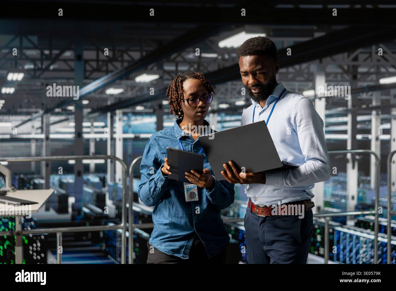 Black software developers on industrial platform analyzing server rigs algorithms in data center, using laptop and tablet. Server room IT specialists collaborating on finetuning PC configurations. Stock Photo