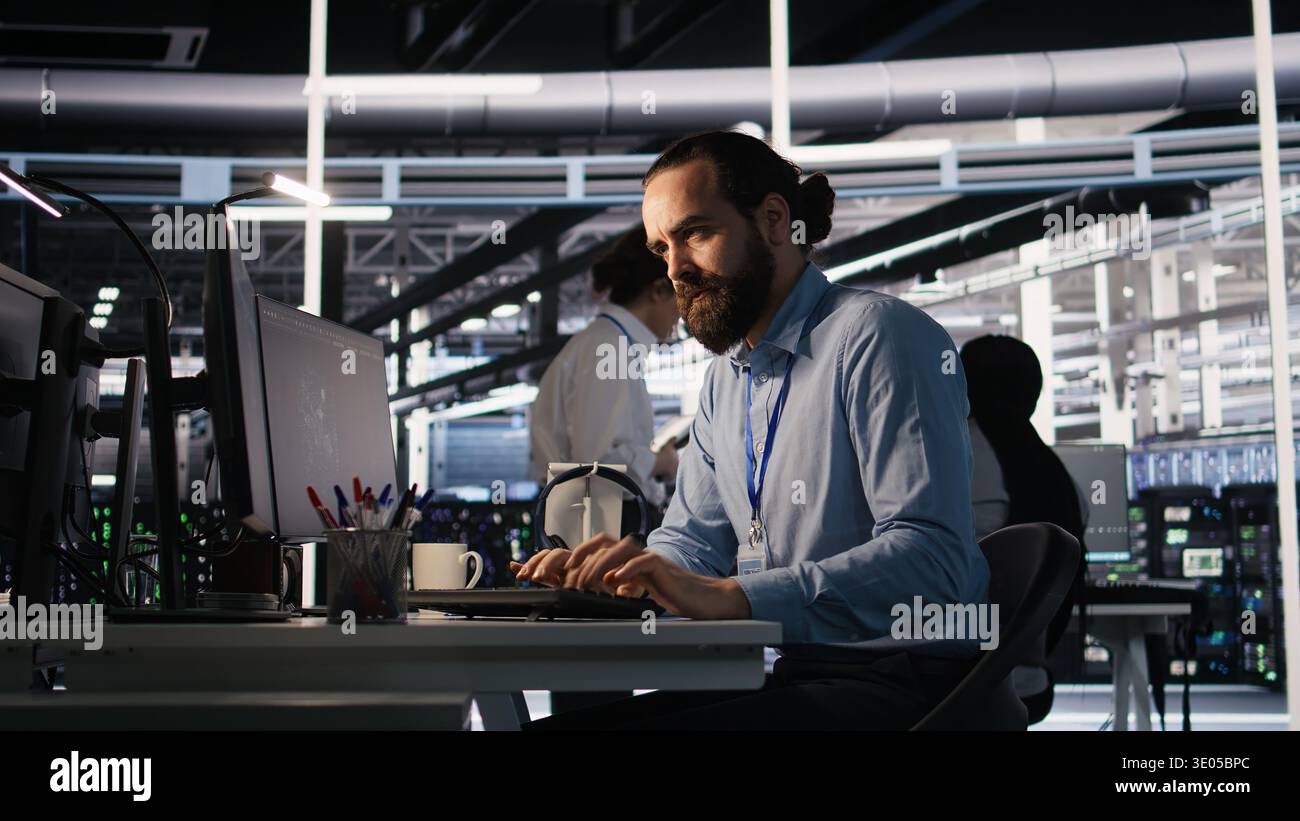 Server room IT specialist frustrated by difficult complex tasks in office. Stressed engineer developing neural network software while working extended hours in data center, camera A Stock Photo