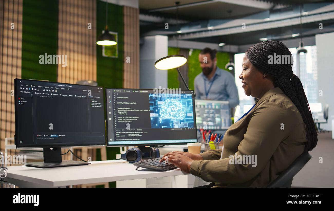 Female technician using computer to write code, developing machine learning APIs. African american woman troubleshooting software errors and faults using artificial intelligence, camera A Stock Photo