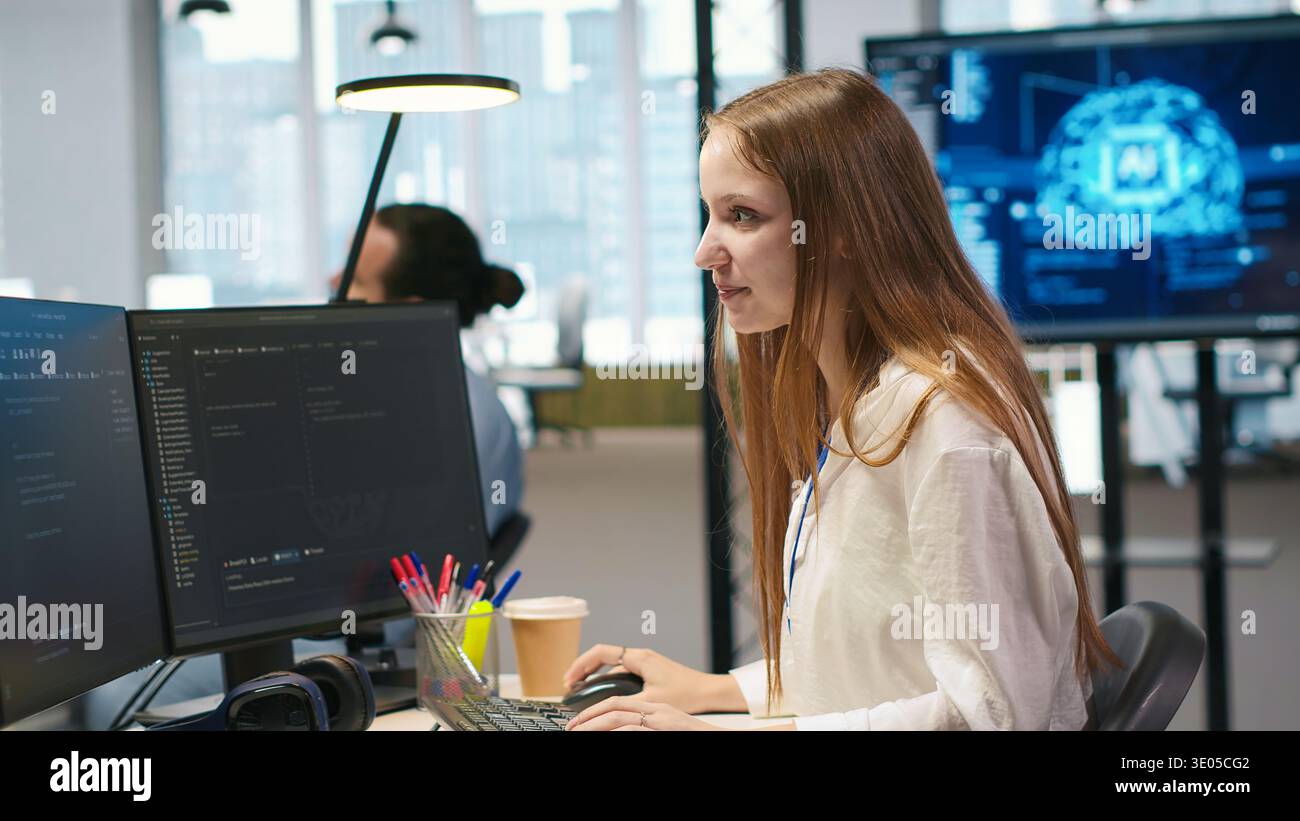 Young female programmer using computer to write code, developing machine learning APIs. Junior developer troubleshooting software errors and faults using artificial intelligence, camera A Stock Photo