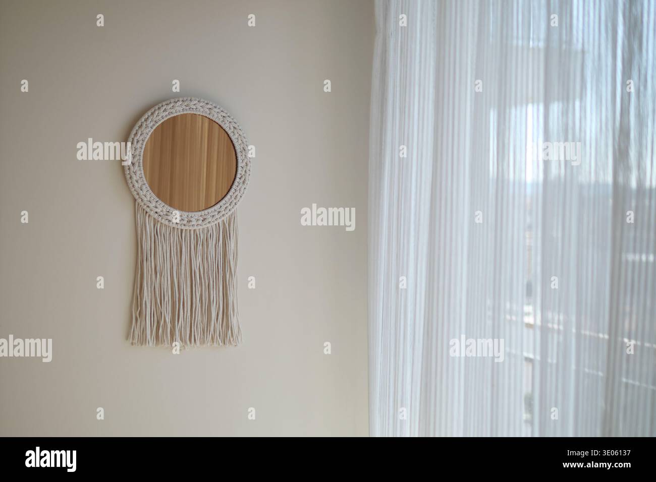 Decorative mirror hangs on wall near white curtain Stock Photo