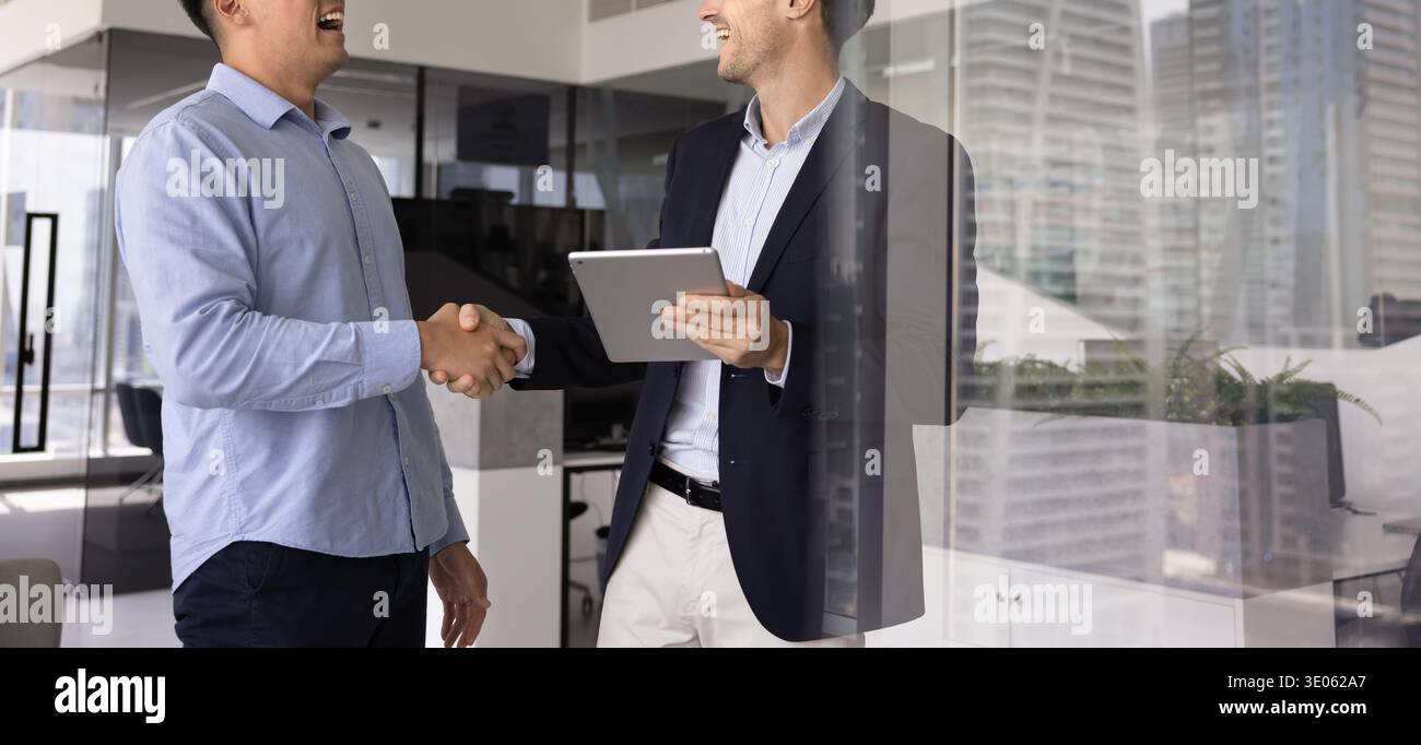 Two multiethnic businessmen holding digital tablet shaking hands in office Stock Photo