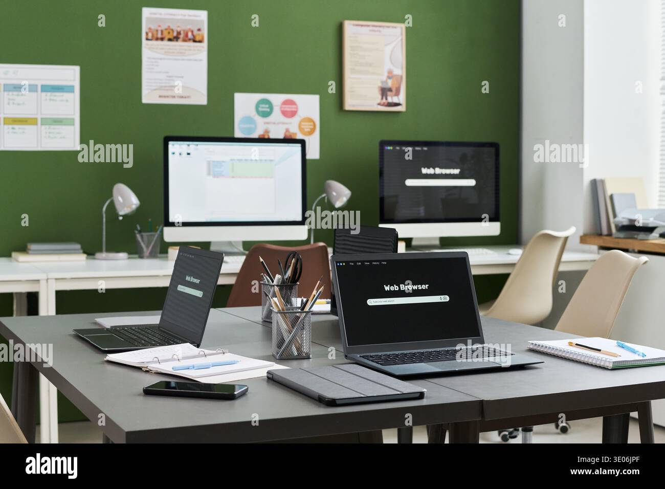 Empty classroom with multiple laptops, tablets, and desktop computers arranged on tables, digital devices displaying web browsers, educational materials suggesting computer literacy course setting Stock Photo