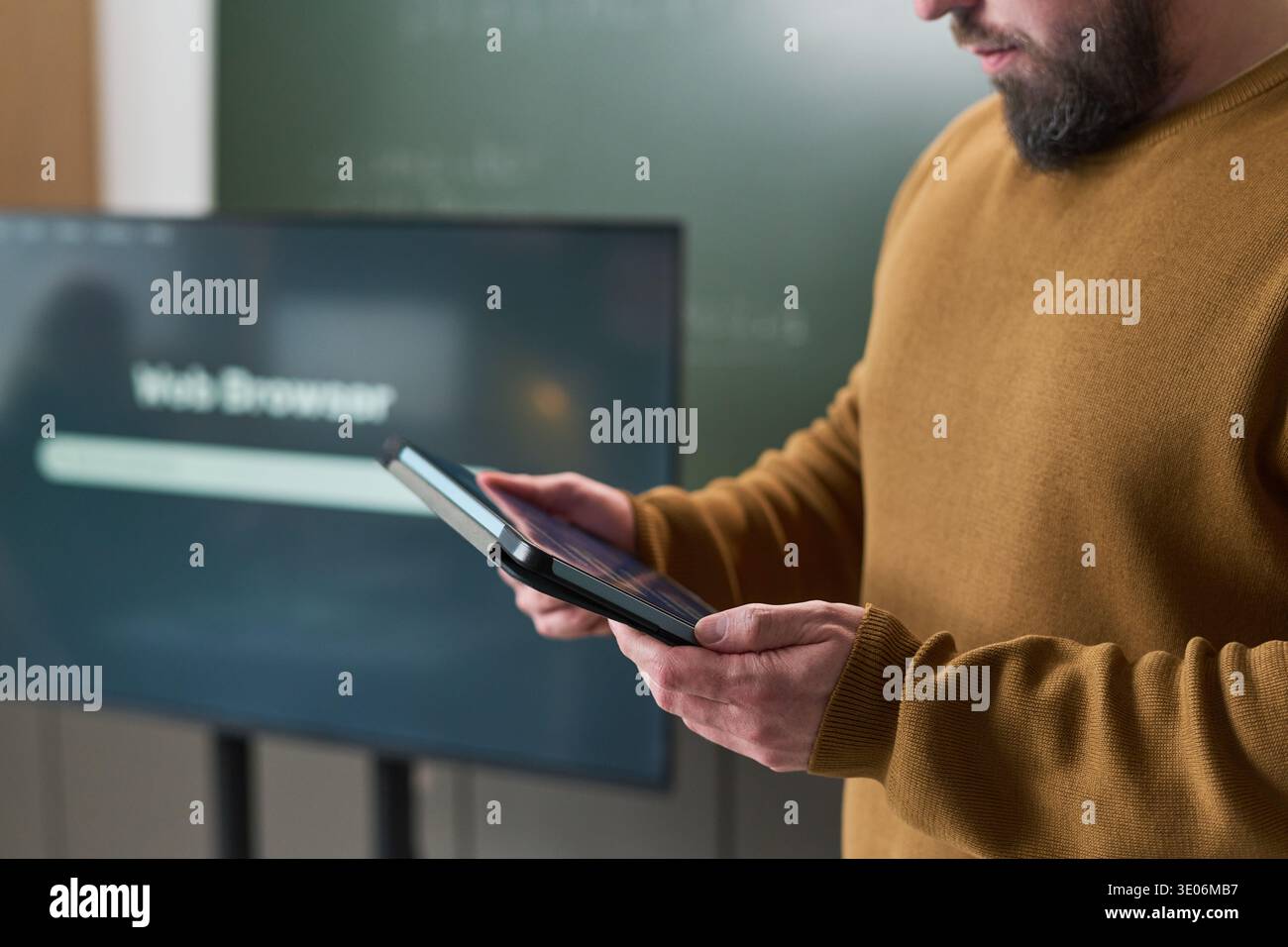 Midsection of man using digital tablet during computer literacy course standing in classroom with interactive display and chalkboard visible in background Stock Photo