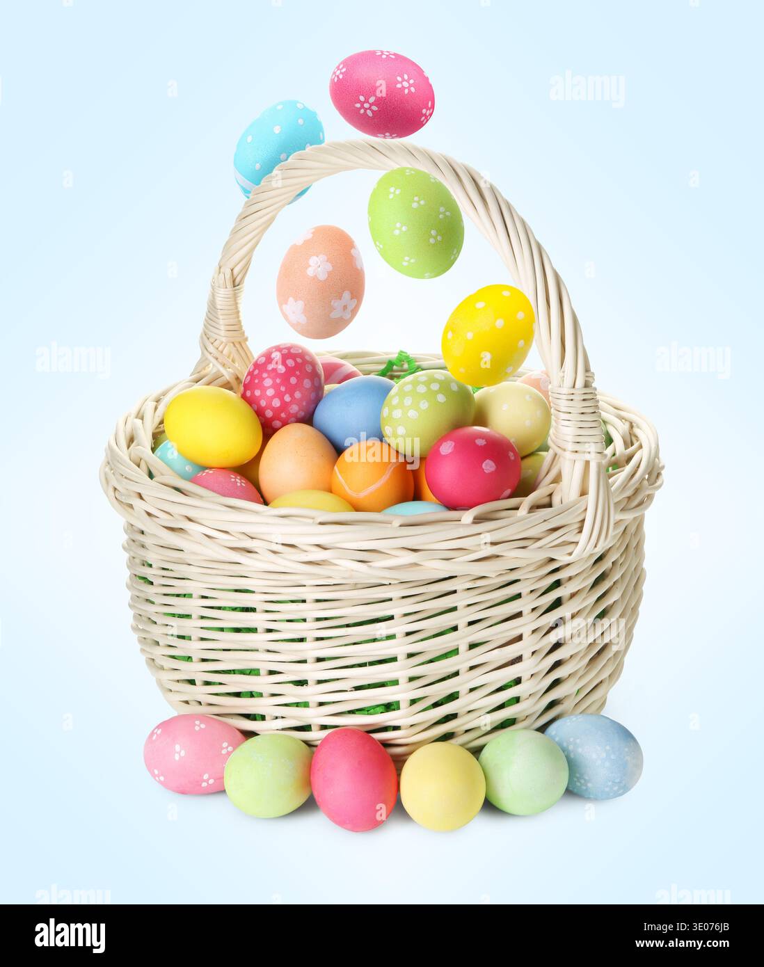 Color Easter eggs falling into basket on light blue gradient background Stock Photo