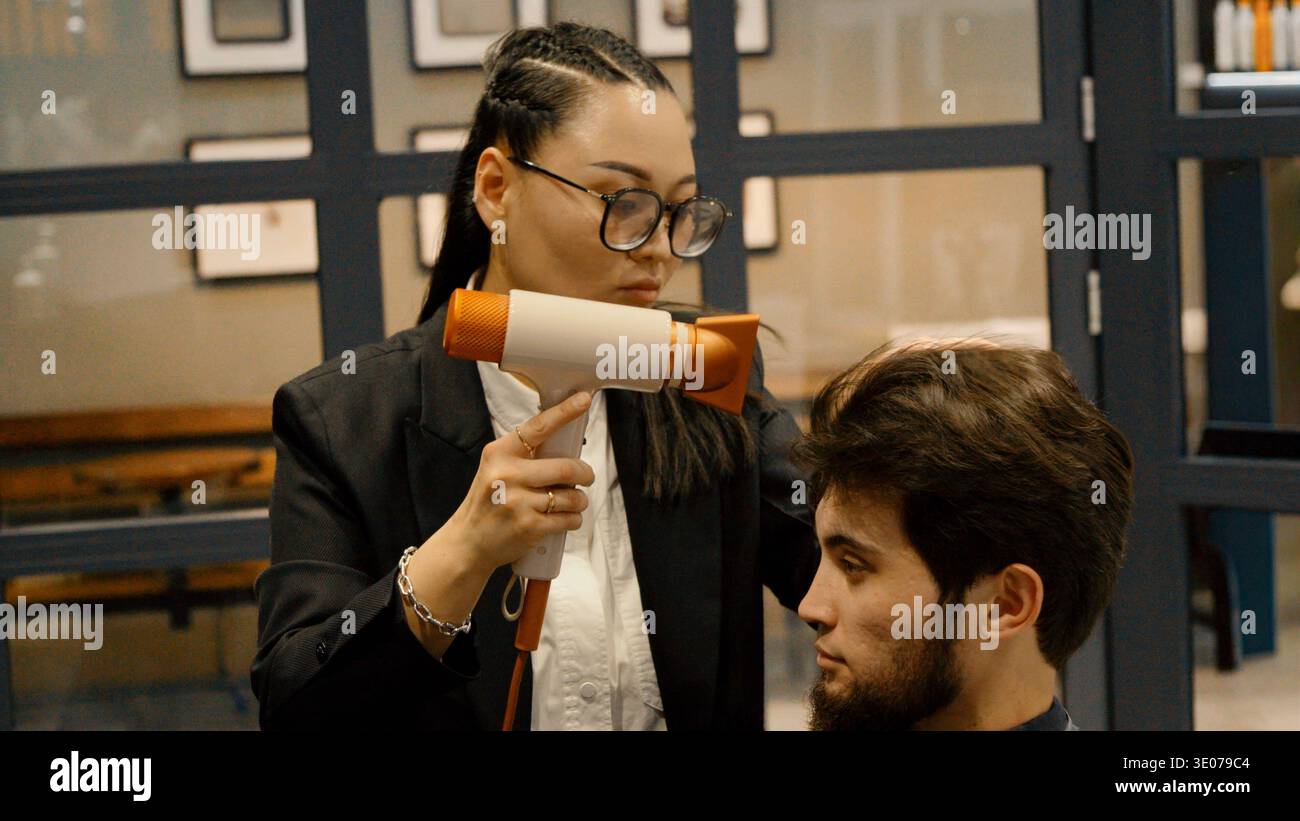 Female barber using a hair dryer for styling a client Stock Photo