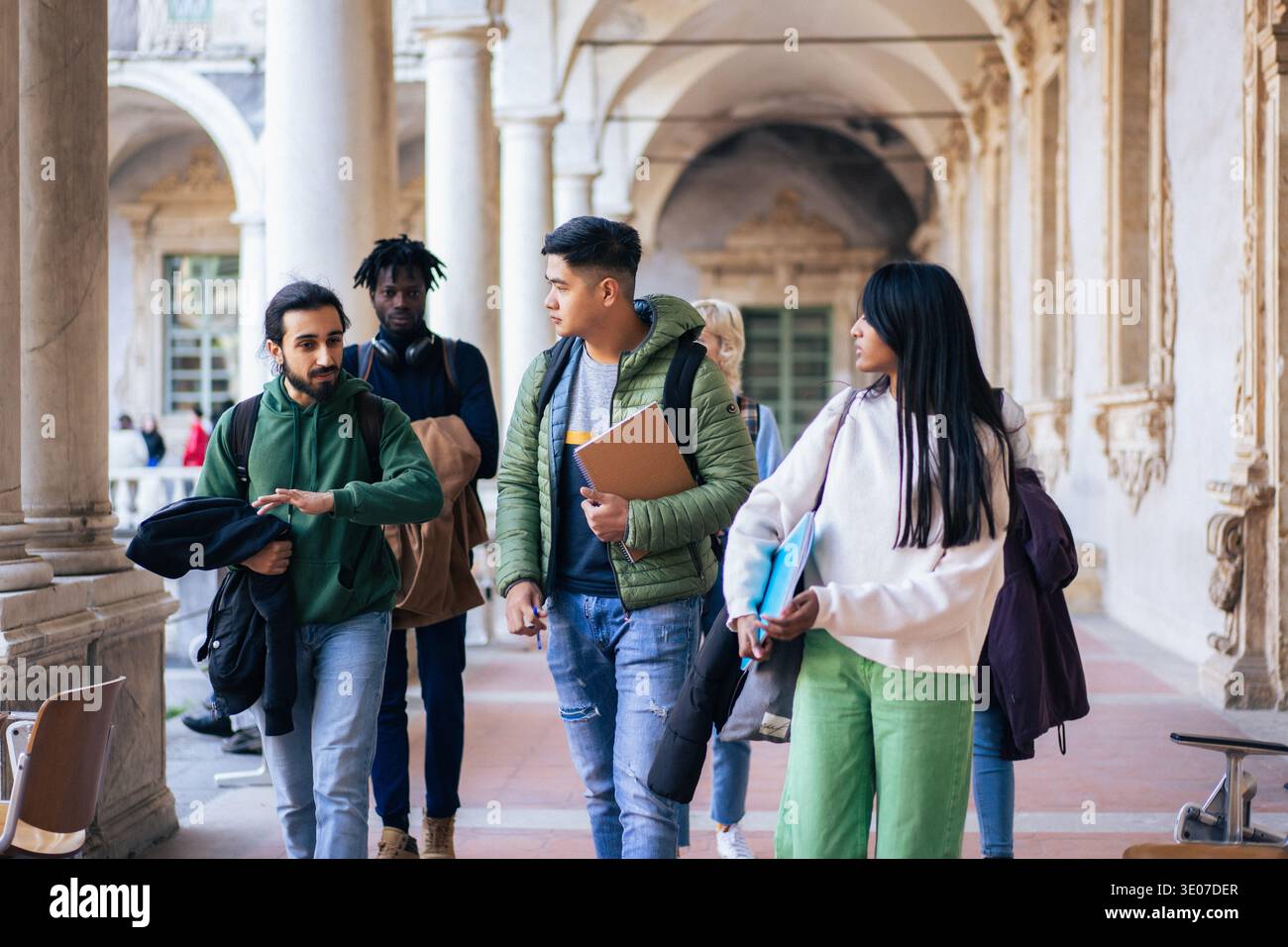 College campus life concept, diverse university students walking through a historic campus corridor between classes. Stock Photo