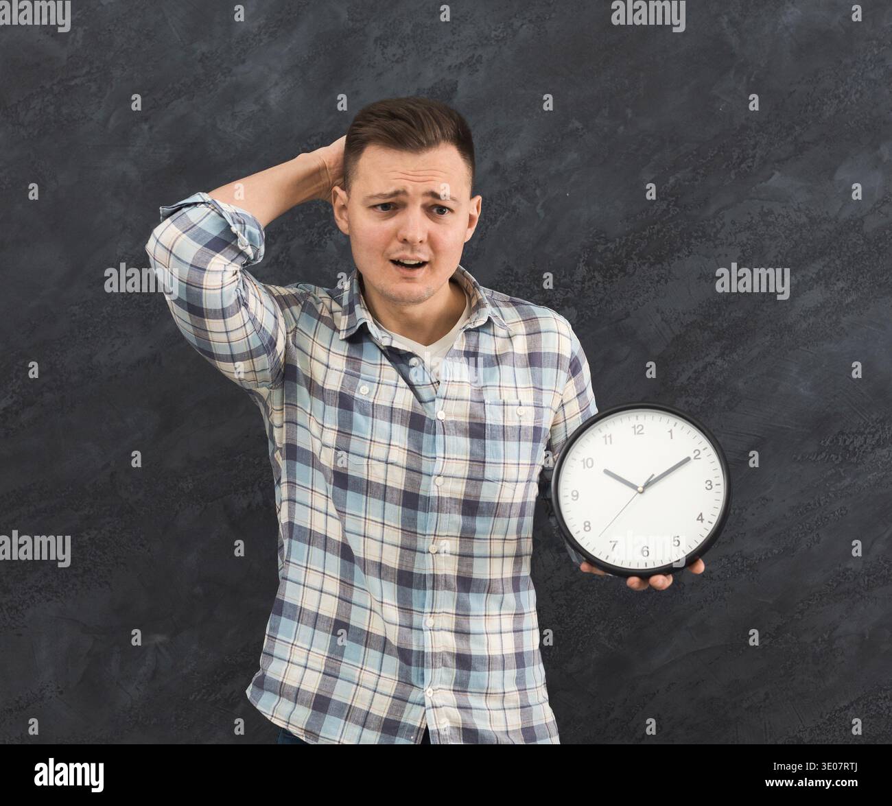 Stressed man holding clock in studio Stock Photo
