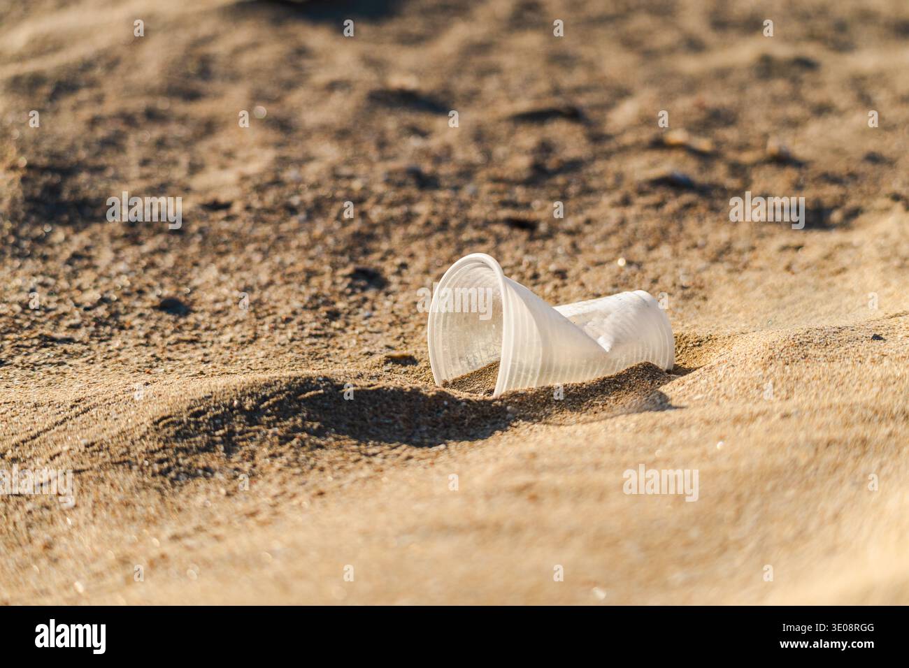 Discarded plastic cup lying on sandy beach symbolizing pollution and environmental problem Stock Photo