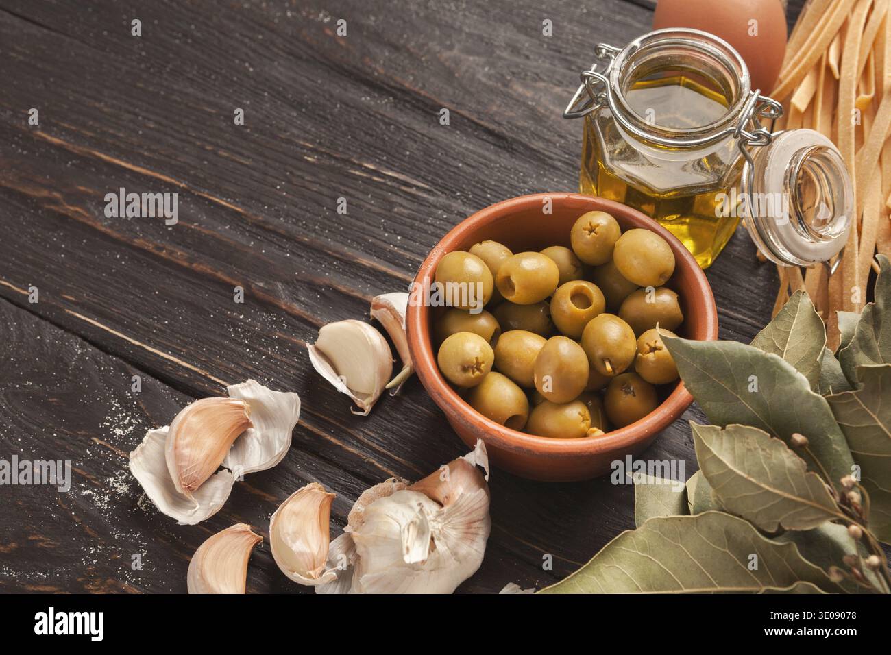 Collection of Olives, Garlic, and Oil Displayed on a Wooden Surface in a Kitchen Setting Stock Photo