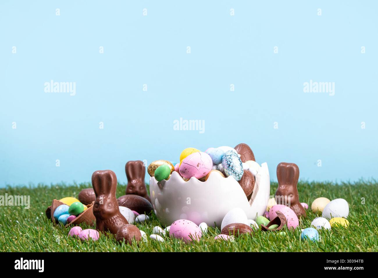 Easter egg hunting background with chocolate eggs. Various candy and chocolate Easter eggs, bunny and rabbits with basket for eggs on green grass park Stock Photo