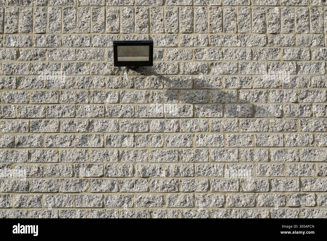 Modern architectural detail. A minimalist gray brick wall featuring a single, rectangular black lamp casting a subtle shadow. Stock Photo