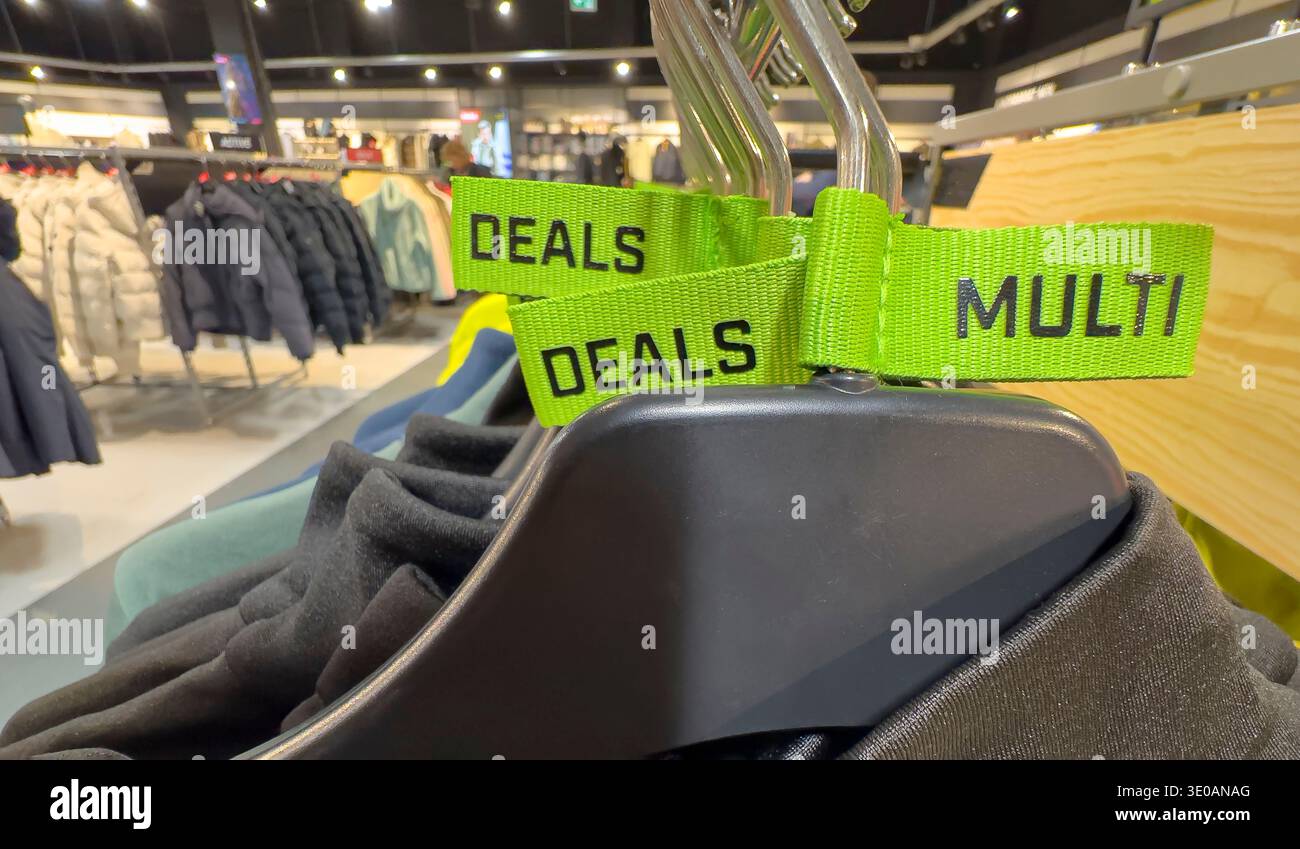 Neon green "Multi Deals" ribbon tags on black clothing hangers in a retail sports apparel store - Smartphone Captured Stock Image