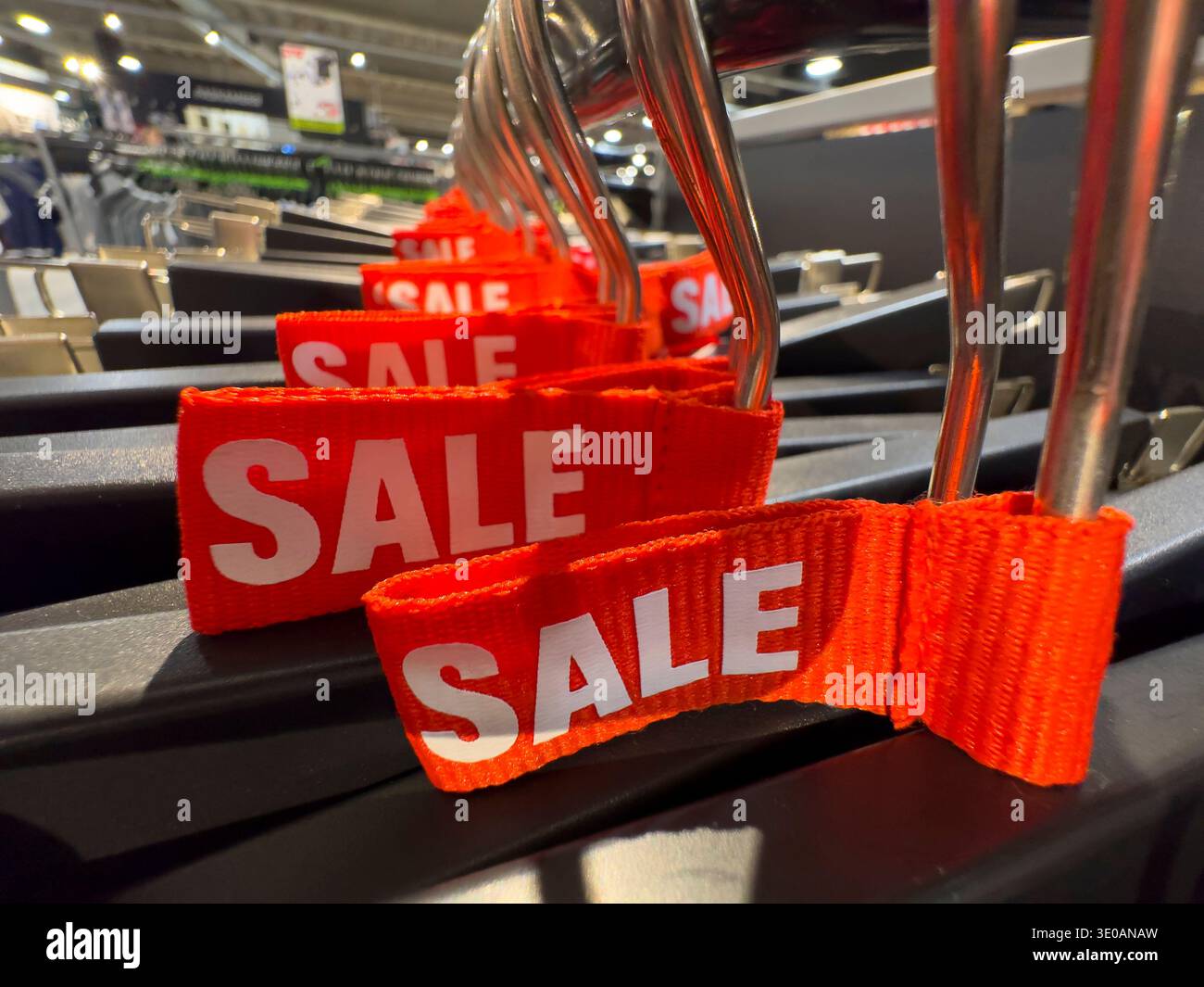 Discounted merchandise with red sale labels on metal hangers in a modern clothing shop interior - Smartphone Captured Stock Image