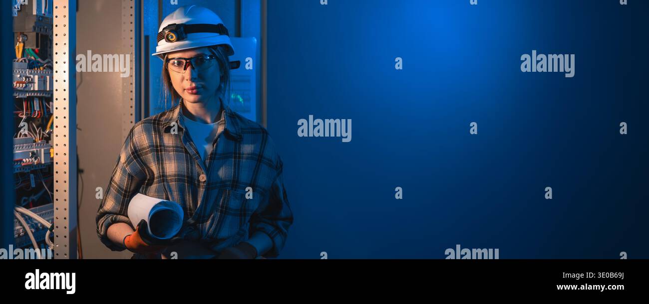 Engineer with blueprints standing near electrical panel in blue light. Engineer energy control. Stock Photo