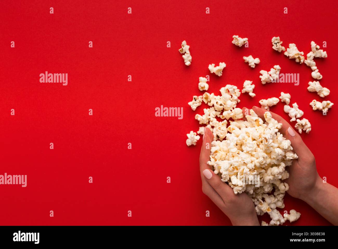 Heap of popcorn in hands on red background, top view Stock Photo