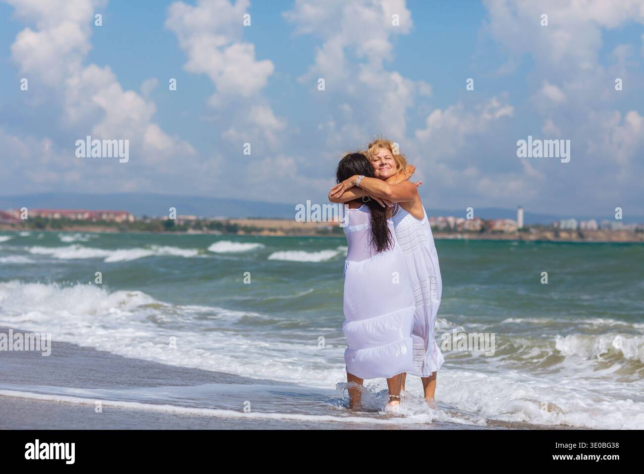 Two Women Hugging on Beach in Ocean Waves Stock Photo