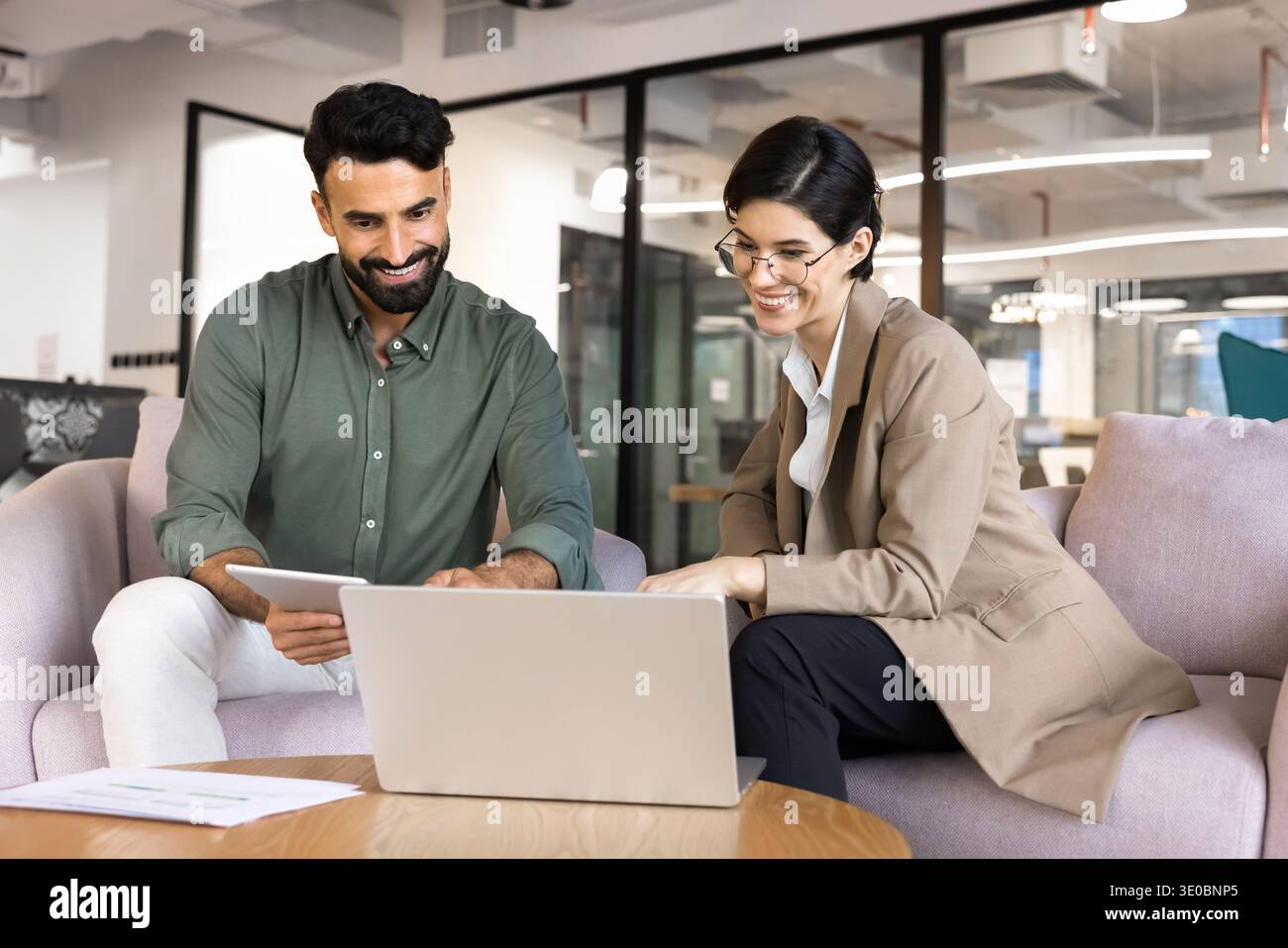 Colleagues collaborating on laptop and digital tablet in office lounge Stock Photo