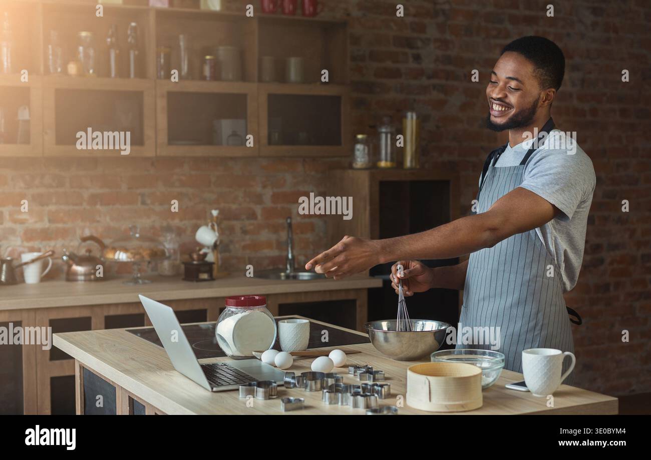 Black man baking pastry and using laptop in kitchen Stock Photo