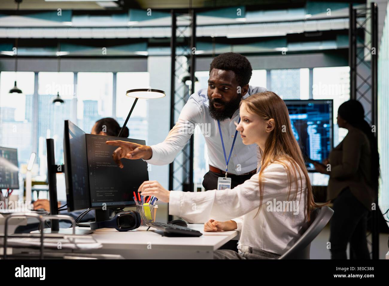 Lead programmer providing support to new worker using PC in software development agency. African american IT expert helping trainee coding during internship in tech startup Stock Photo