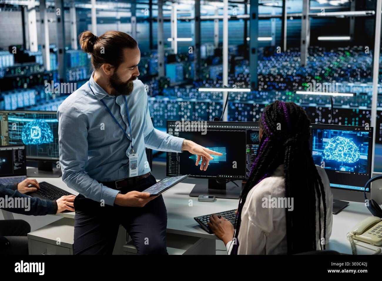 Manager supervising female engineer in data center coding with generative AI assistance. Supervisor oversees work by IT specialist leveraging artificial intelligence large language model Stock Photo