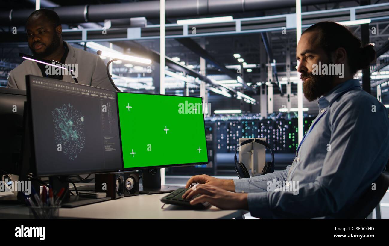 Data center technician doing software updates using green screen mockup computer. Server room IT specialist , optimizing infrastructure using chroma key isolated screen PC, camera A Stock Photo