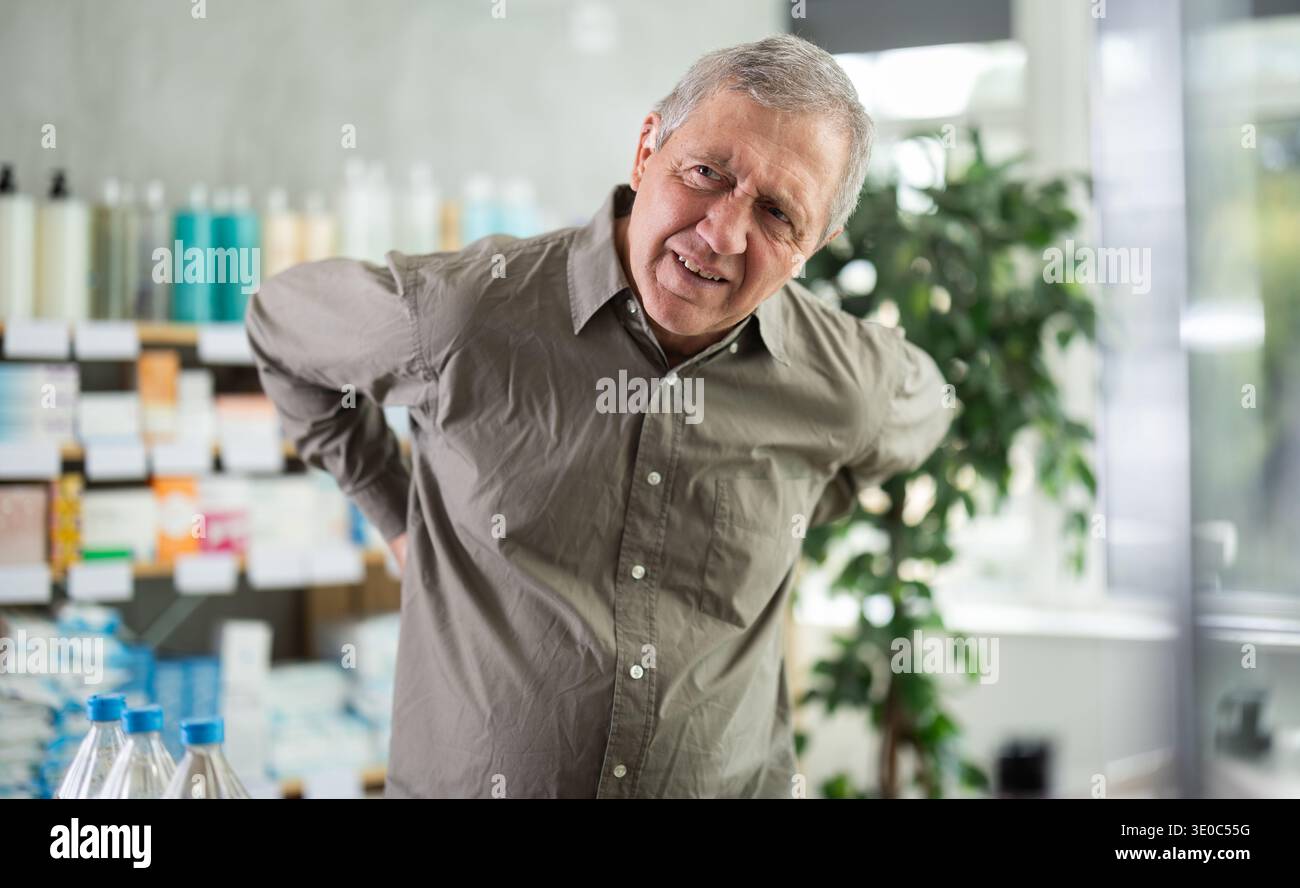 Older man experiencing sharp back pain while shopping in pharmacy Stock Photo