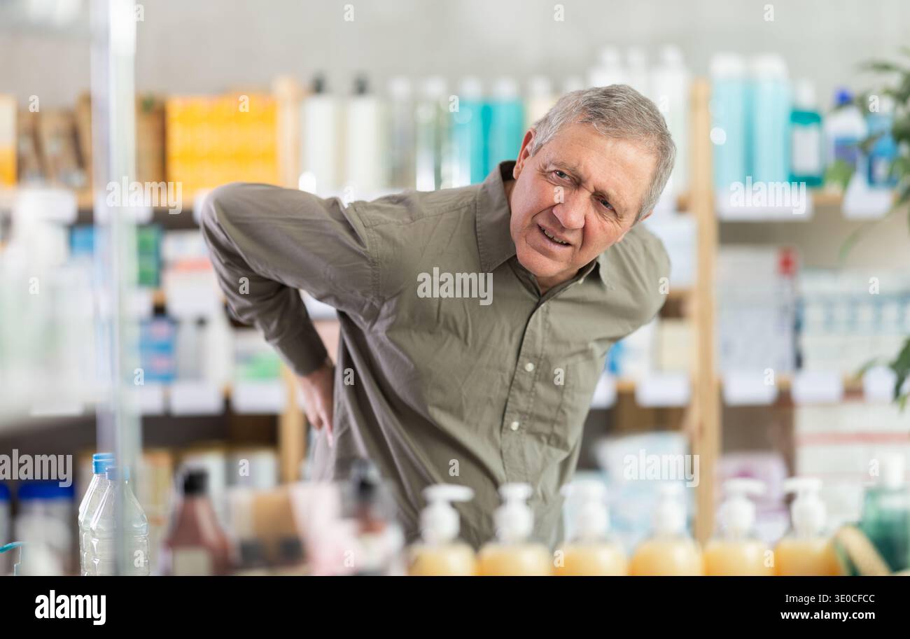 Older man experiencing sharp back pain while shopping in pharmacy Stock Photo