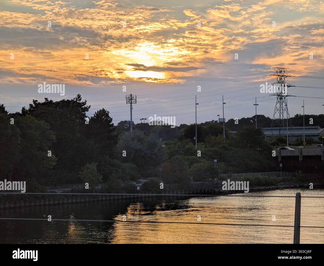 Dramatic Golden Sunset over Humber River, Toronto. High-voltage power lines and utility towers silhouetted against a vibrant cloudy sky at dusk. - Smartphone Captured Stock Image