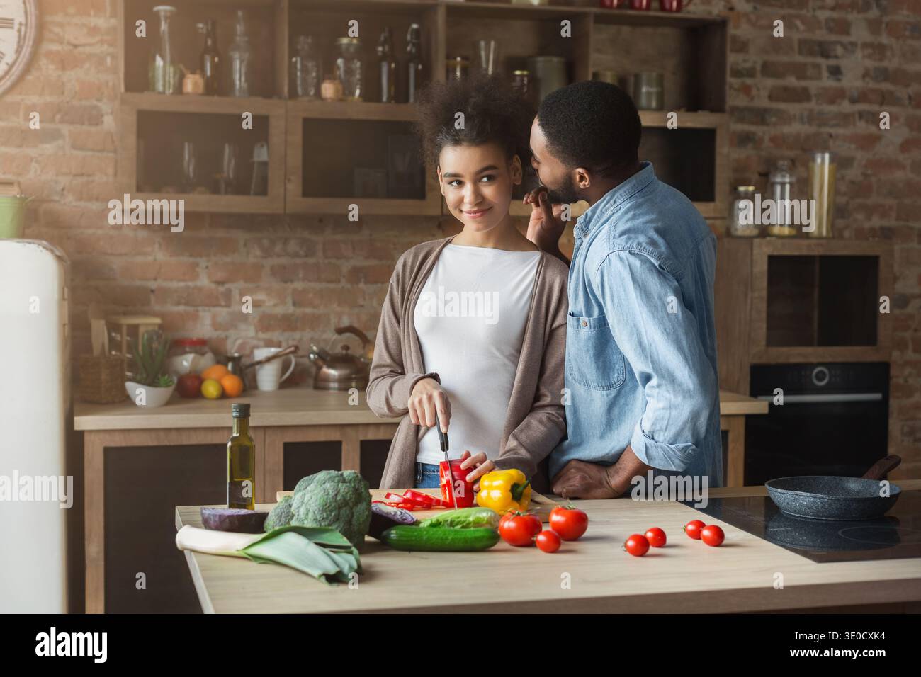 Man whispering in wife's ear while cooking Stock Photo