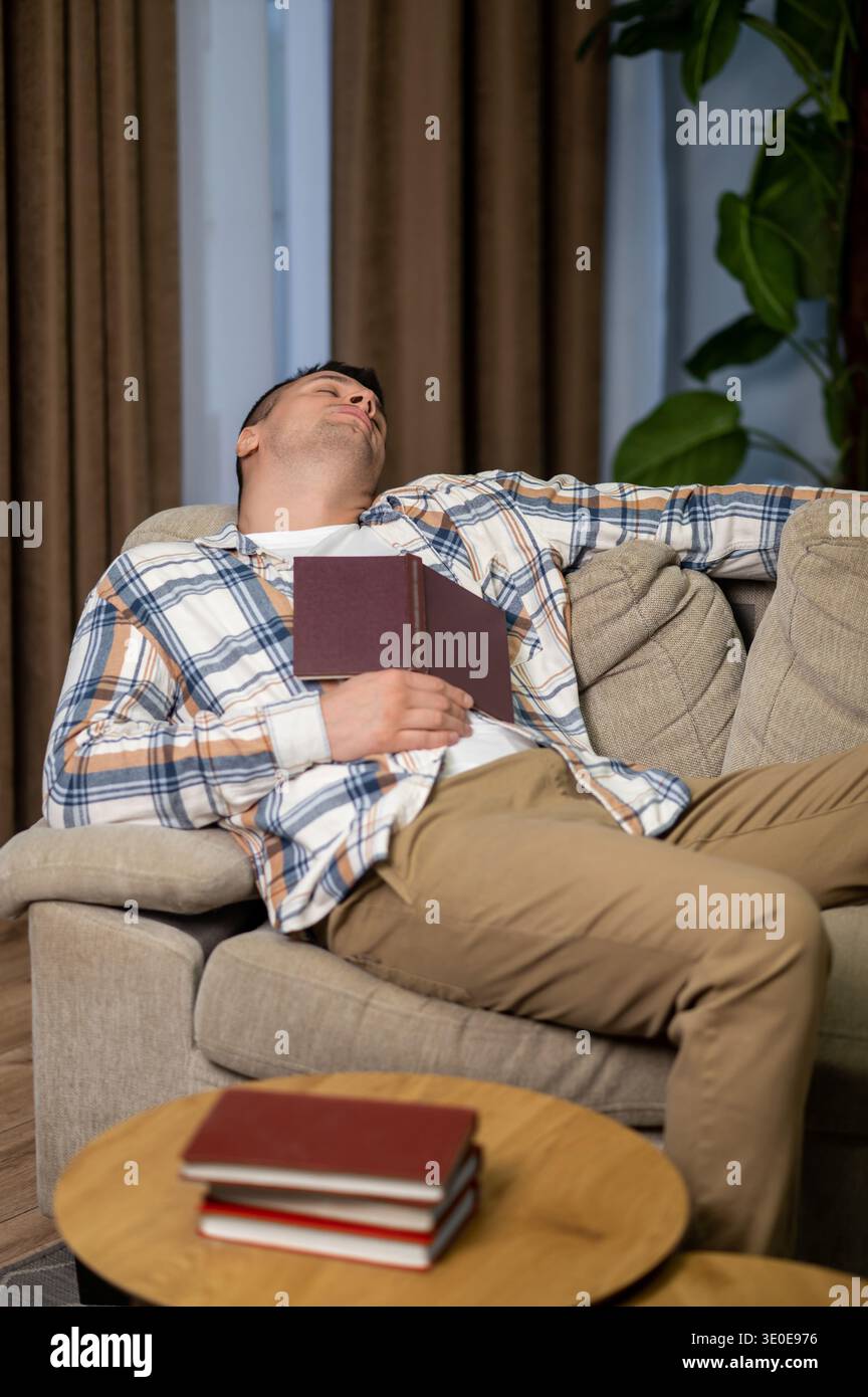 Tired man sleeping with book on sofa in modern living room interior Stock Photo