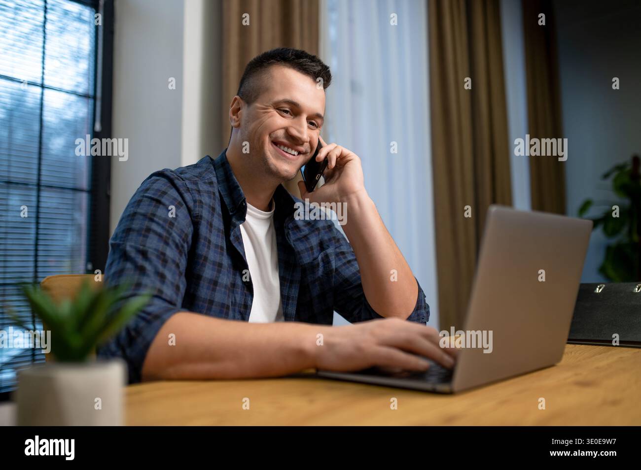 Happy man speaking on phone and working on laptop in contemporary office Stock Photo