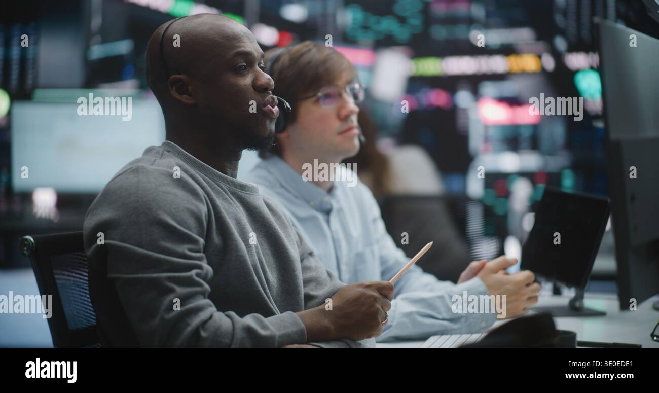 Seasoned African American Financial Expert Provides Hands on Training to Young Male Colleague. Men Deeply Engaged in Analyzing Real Time Data on Digital Tablet and Monitors. Mentorship, Tech Training. Stock Photo