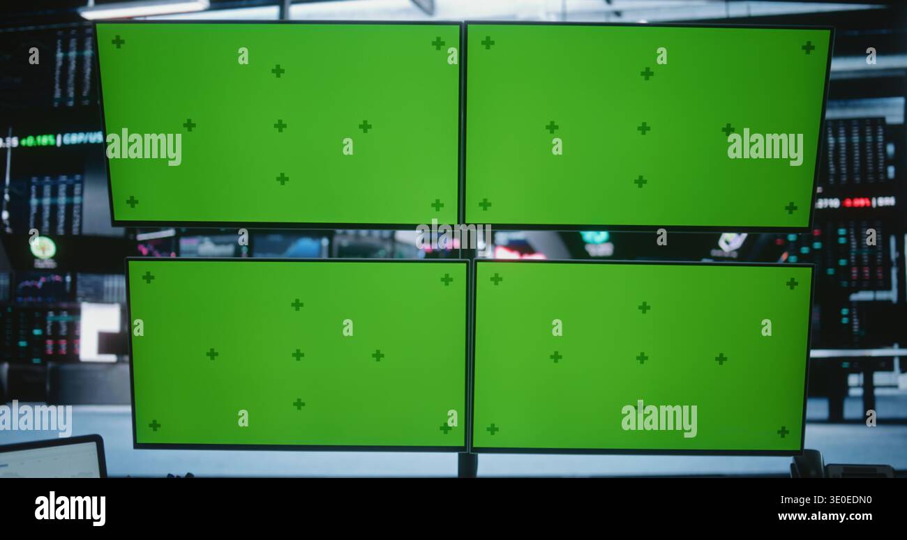 African American Male Trader Working at Modern High Tech Desk With Four Green Screen Monitors in Busy Financial Office. Concept of Financial Data, Software Demos, and Corporate Presentations. Stock Photo