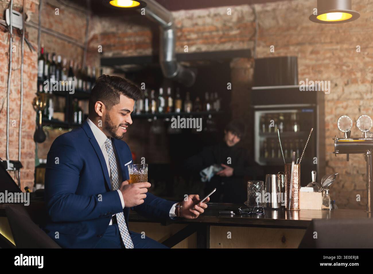 Young man sitting at bar counter and using smartphone Stock Photo