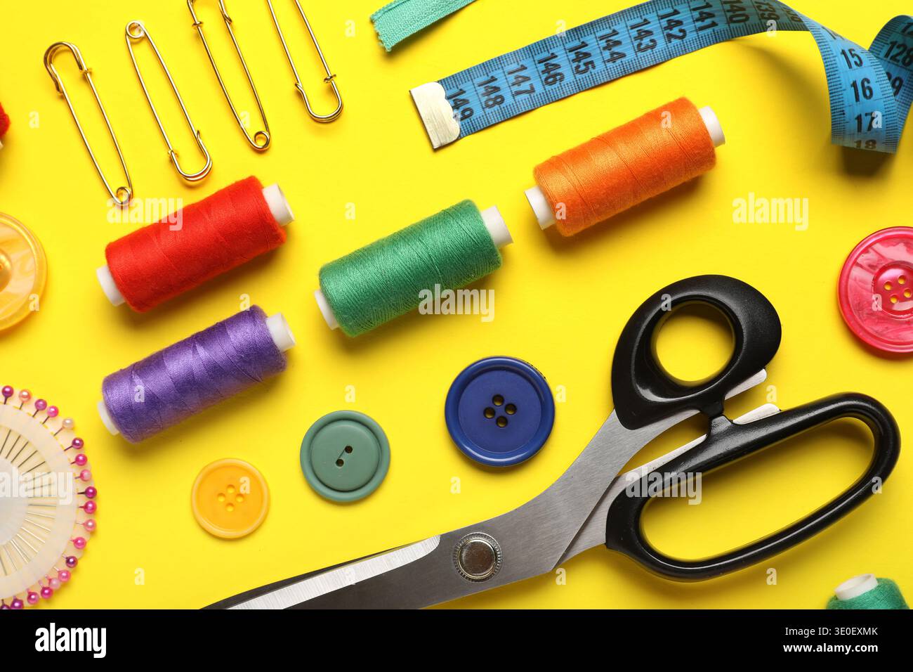 Composition with different thread spools and sewing accessories on yellow background, closeup Stock Photo