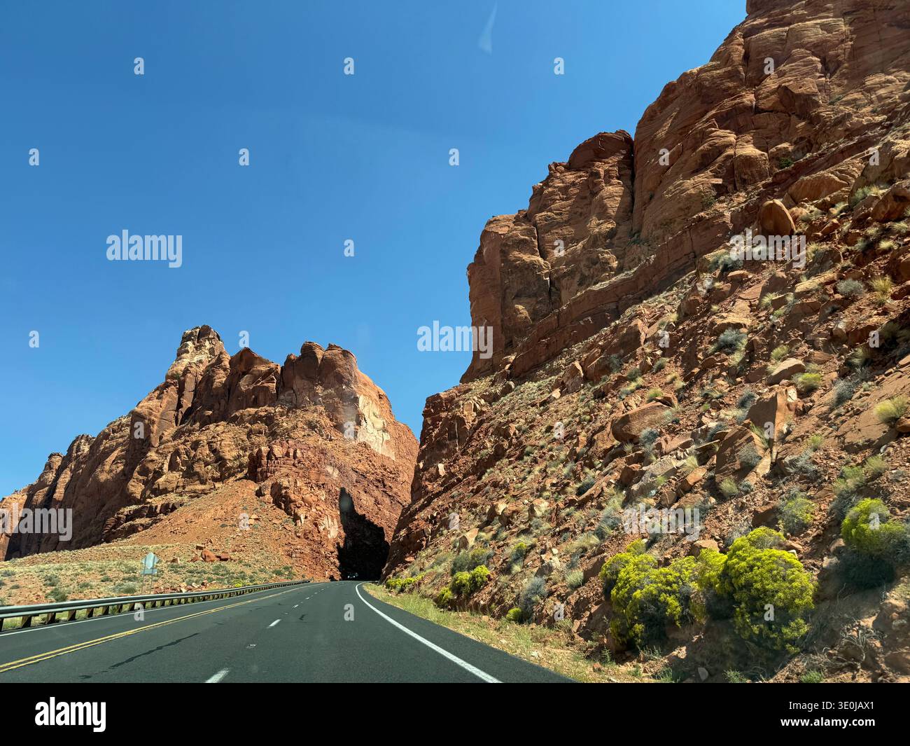 Highway cutting through towering red rock canyon walls in Utah desert with car driving along scenic route, USA. - Smartphone Captured Stock Image