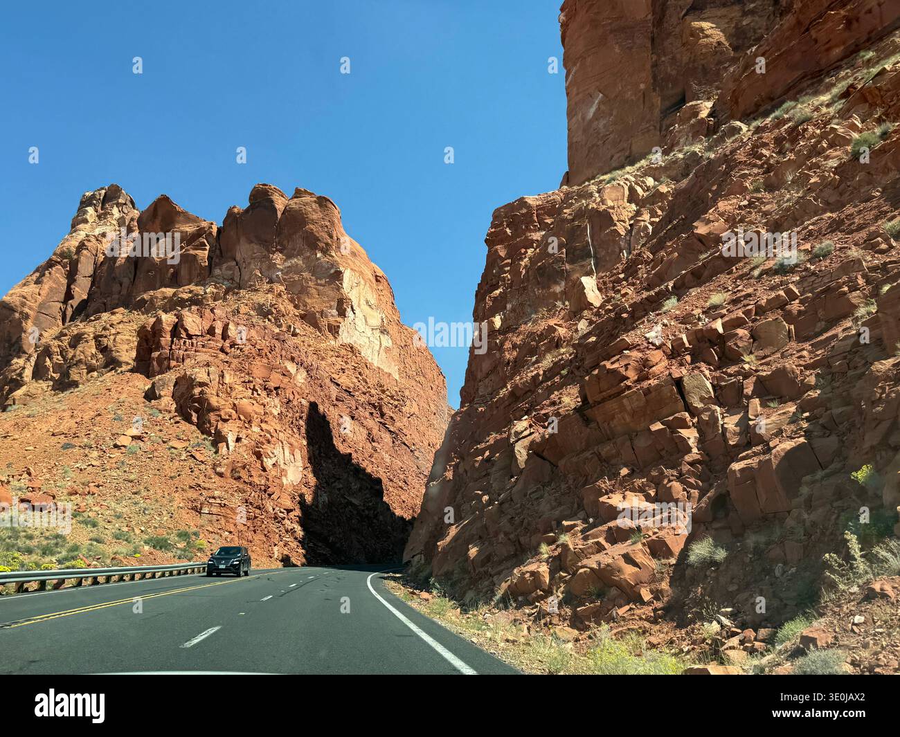 Highway cutting through towering red rock canyon walls in Utah desert with car driving along scenic route, USA. - Smartphone Captured Stock Image