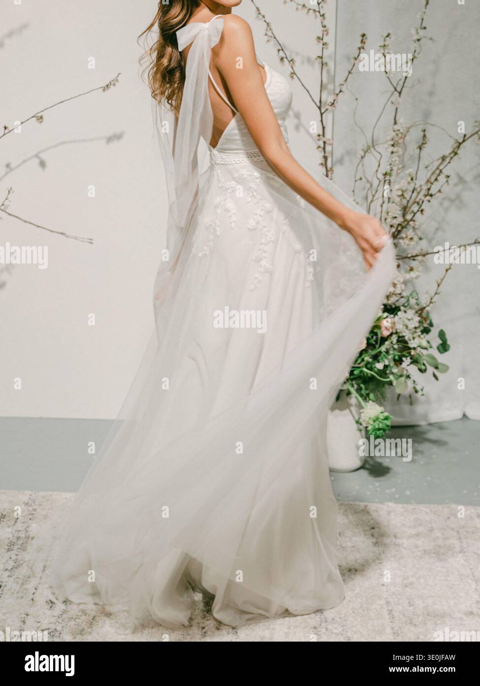 A bride poses in a light wedding dress with a veil in a studio. She stands  beside a floral arrangement and branches while softly holding the dress  Stock Photo - Alamy