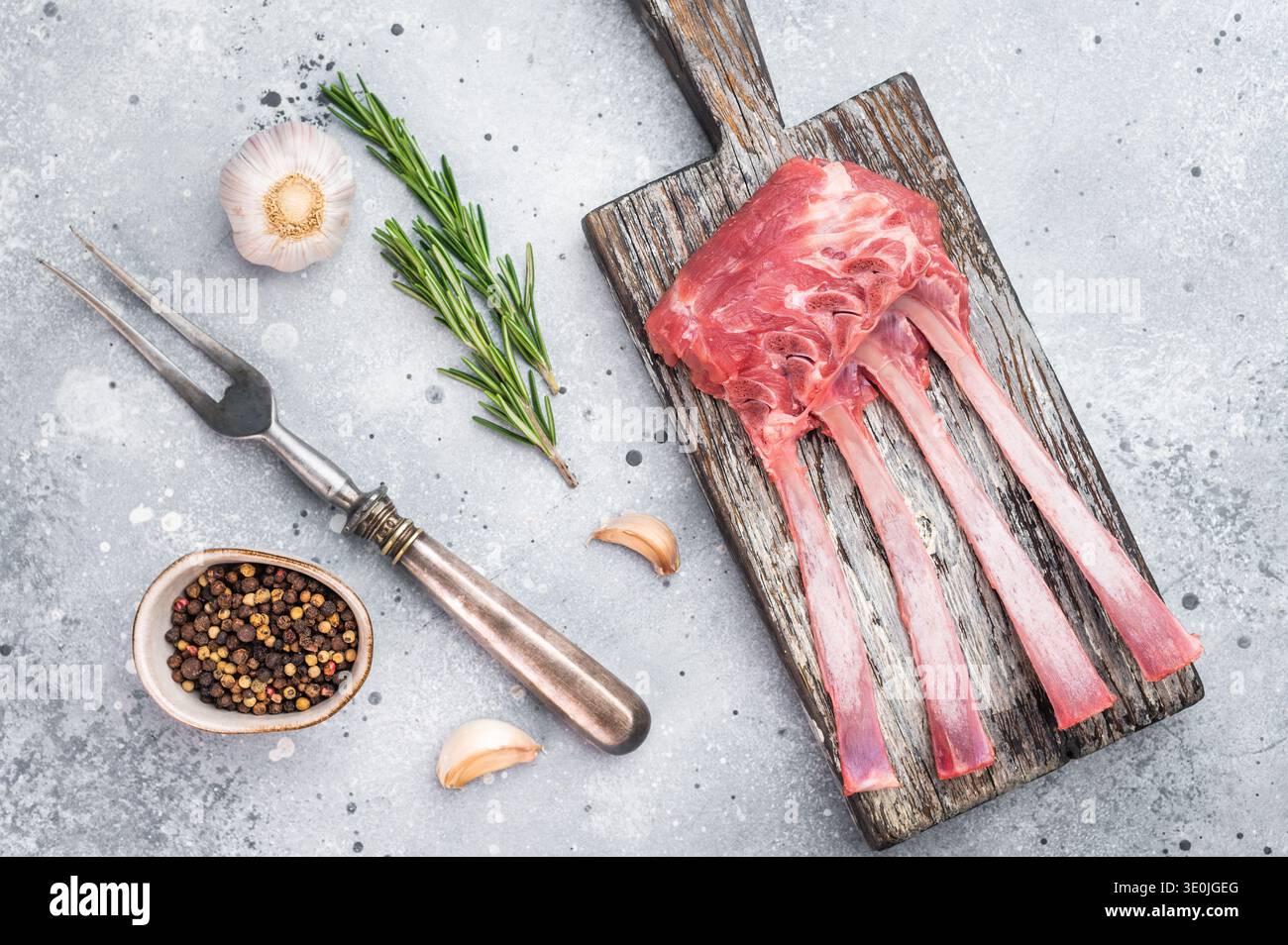 Uncooked lamb ribs and cutlets with herbs and spices on wooden board stone background top view butcher preparation. Stock Photo