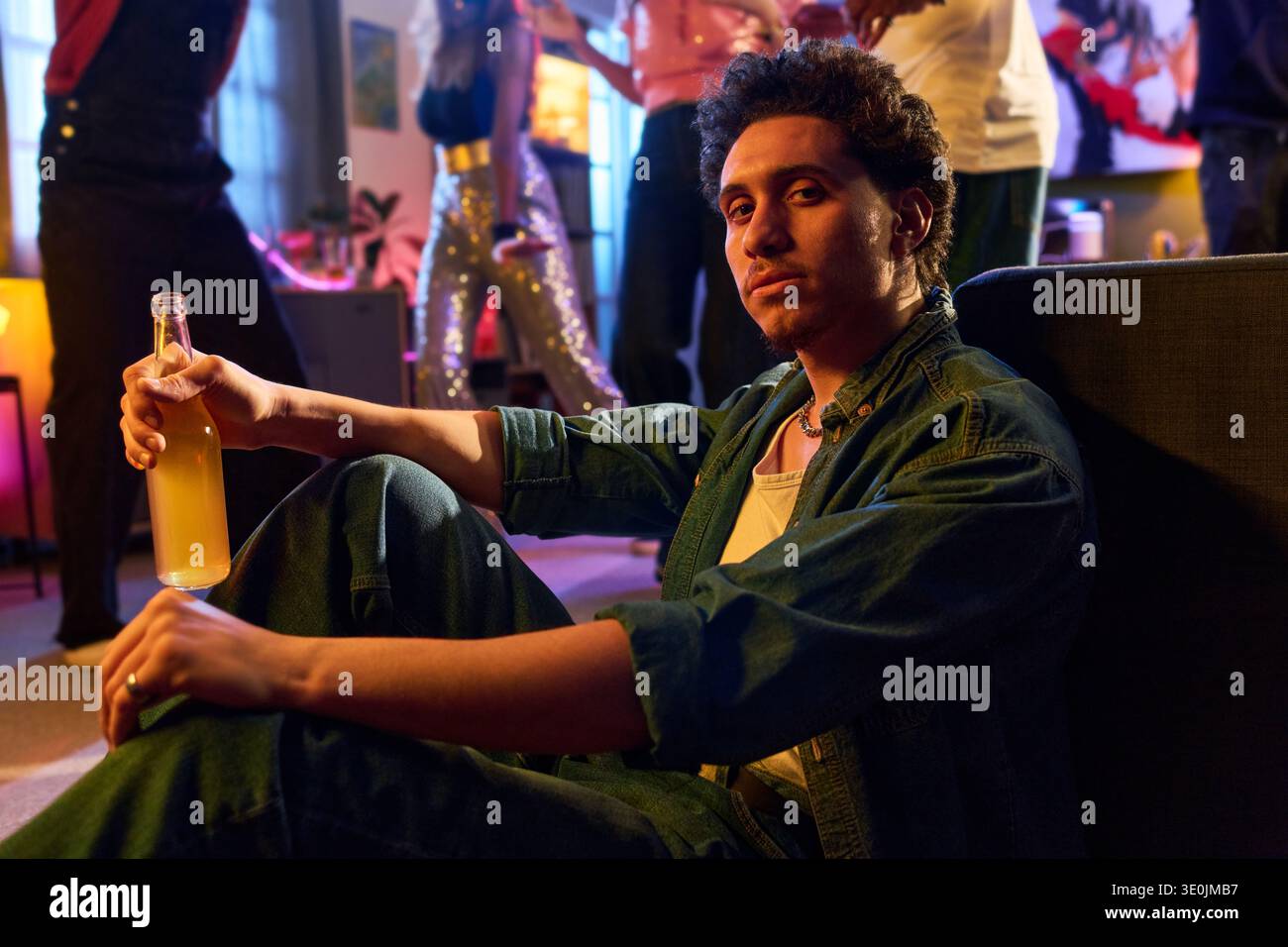 Portrait of young Hispanic Man Sitting on Floor Holding Drink at Party Stock Photo