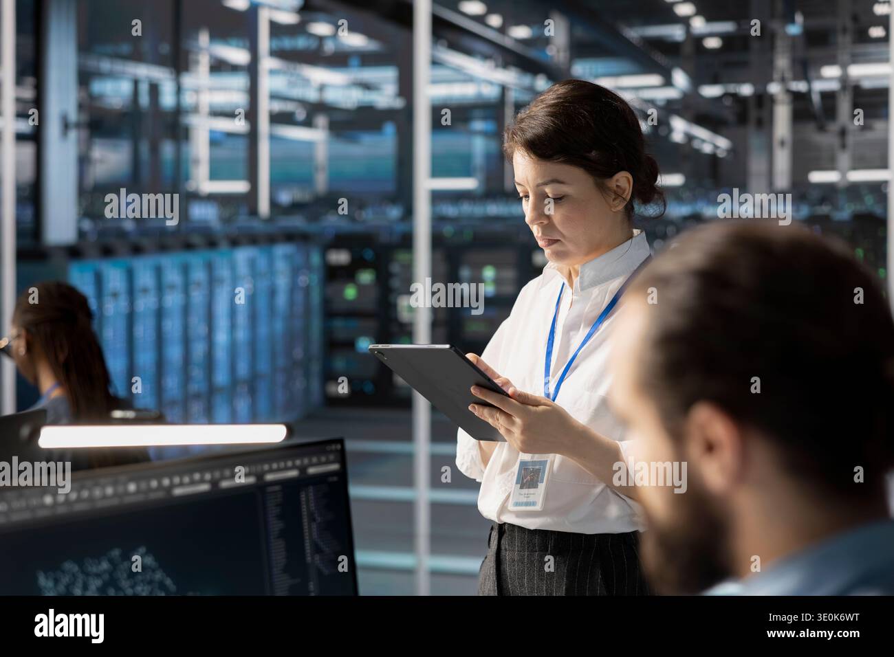 Engineers using tablet in data center, managing server virtualization, running scripts. Woman in server farm using programming language on device to finetune network protocols Stock Photo