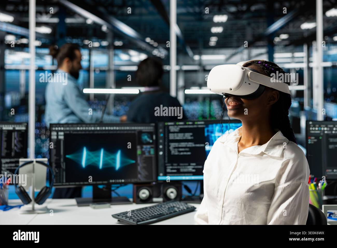 Smiling engineer using virtual reality, optimizing performance with AI assistant analysis. Cheerful data center female developer wearing VR headset, speed up tasks with LLM chatbot Stock Photo