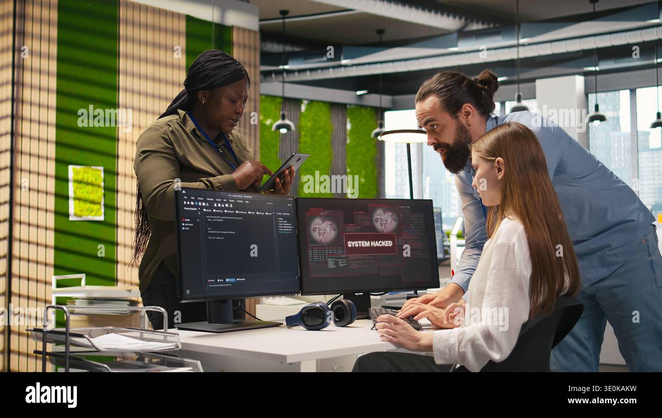 Young programmer in office requests help from IT experts detecting and blocking hacker intrusion. Intern assisted by staff members coordinating incident response for network attack, camera A Stock Photo