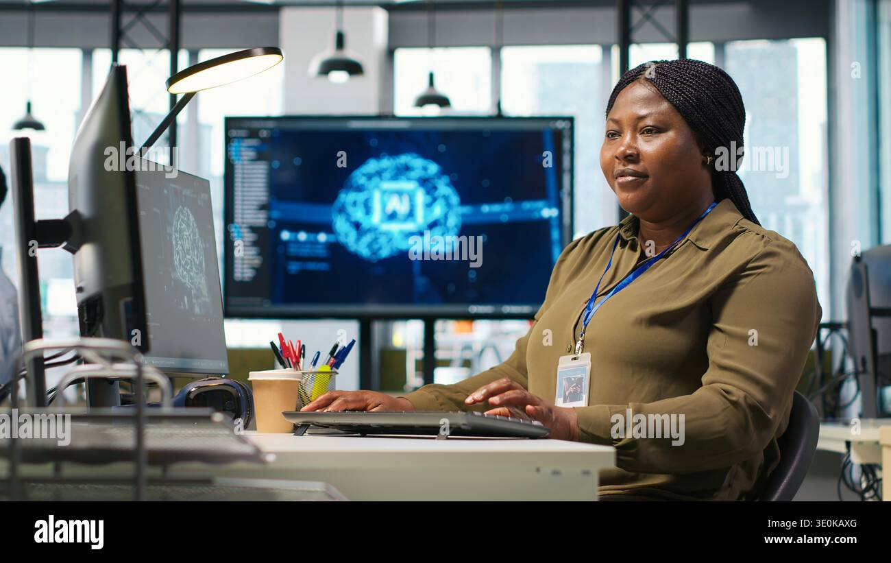 Female technician using computer to write code, developing machine learning APIs. African american woman troubleshooting software errors and faults using artificial intelligence, camera A Stock Photo