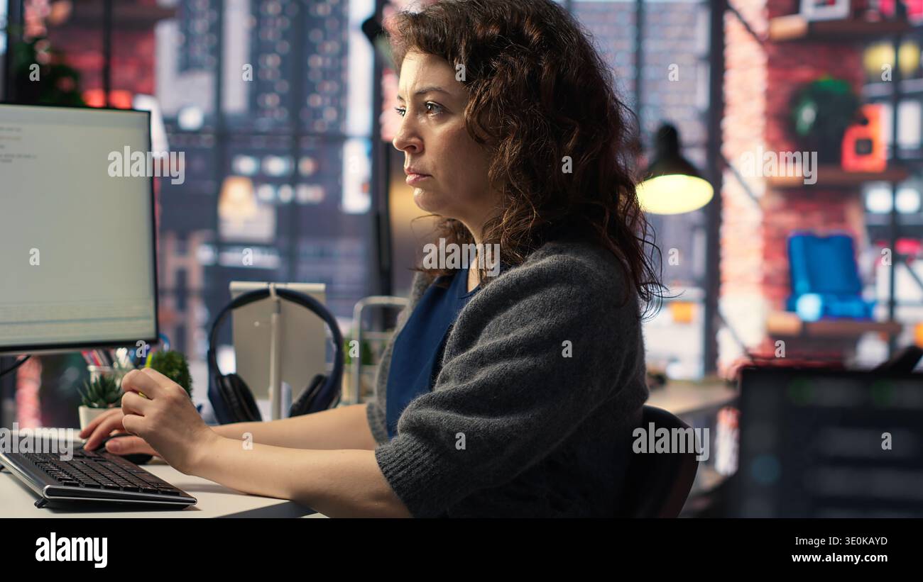 Young woman programming software code on her computer, using coding language for debugging tasks. Workspace with dual monitors helps with software engineering and web development. Camera B. Stock Photo