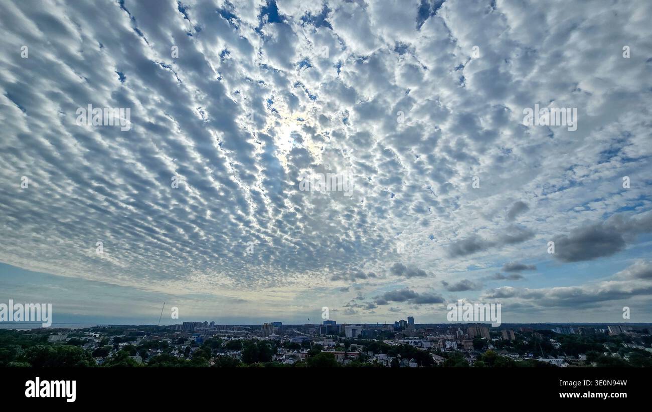 Wide city skyline under dramatic textured cloud pattern with sunlight breaking through bright sky. Stock Photo