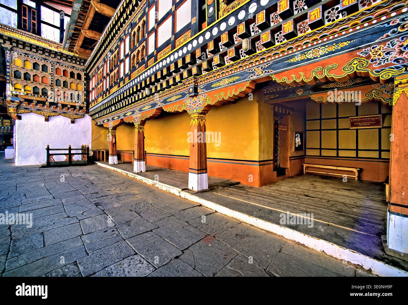 The photo shows a Bhutanese temple featuring colorful architecture. The stone courtyard is part of a Dzong, likely the chamber of a governor. Stock Photo
