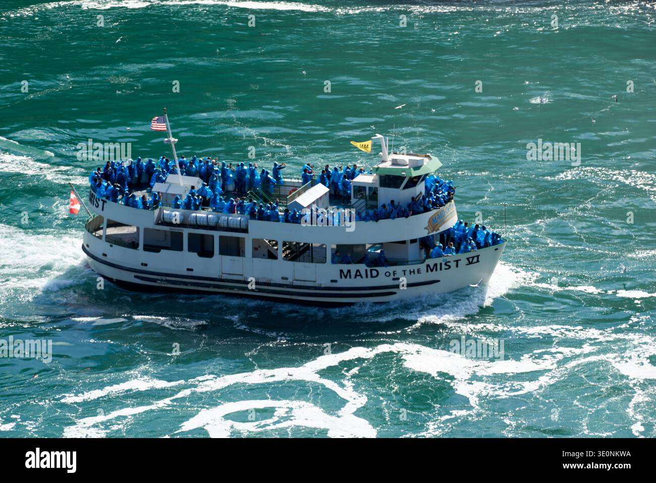 Tourists in blue ponchos ride the Maid of the Mist VI boat at Niagara Falls, experiencing the iconic natural wonder up close. Stock Photo